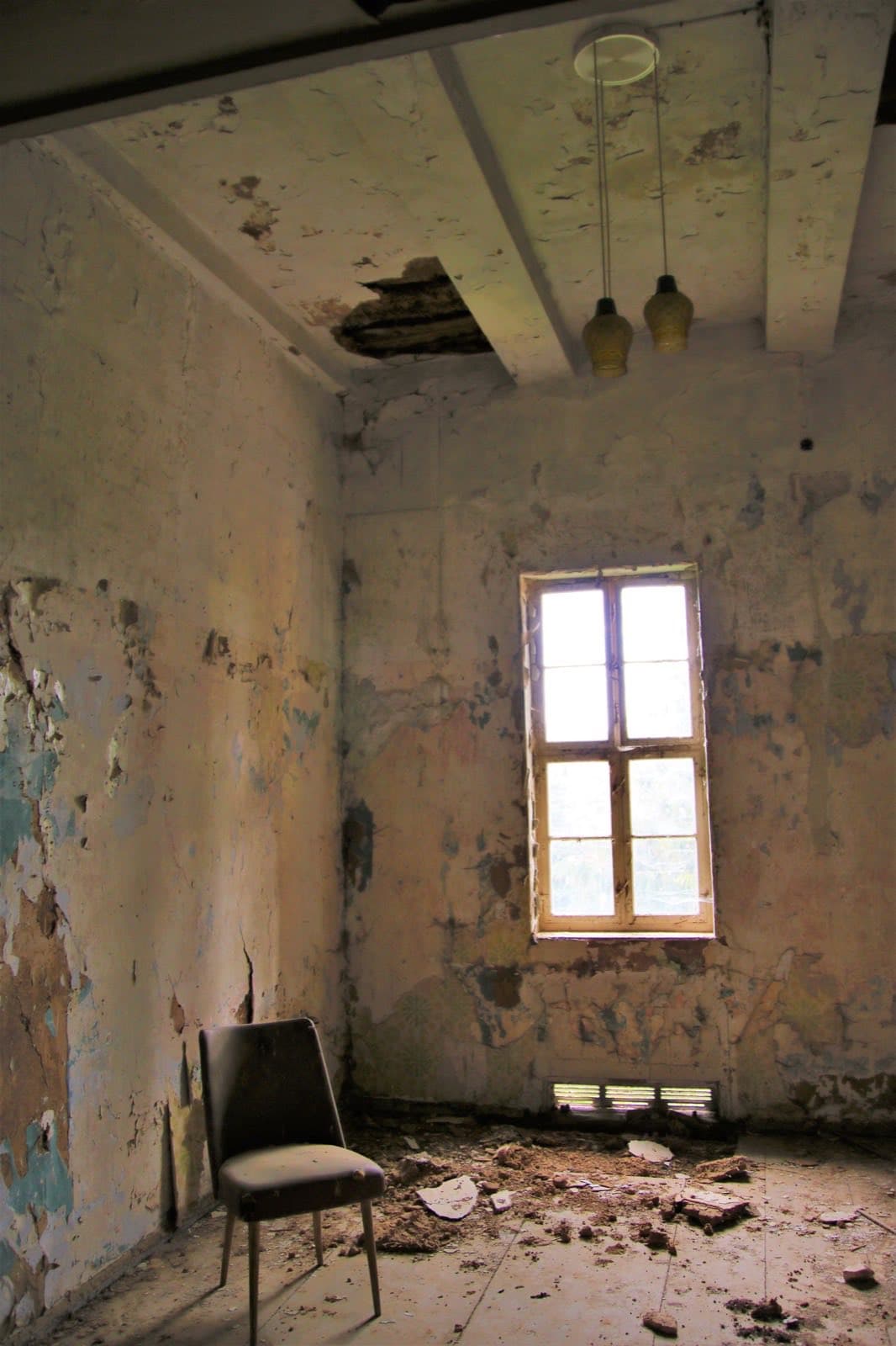 Empty room with a hole in the ceiling and peeling paint on the walls