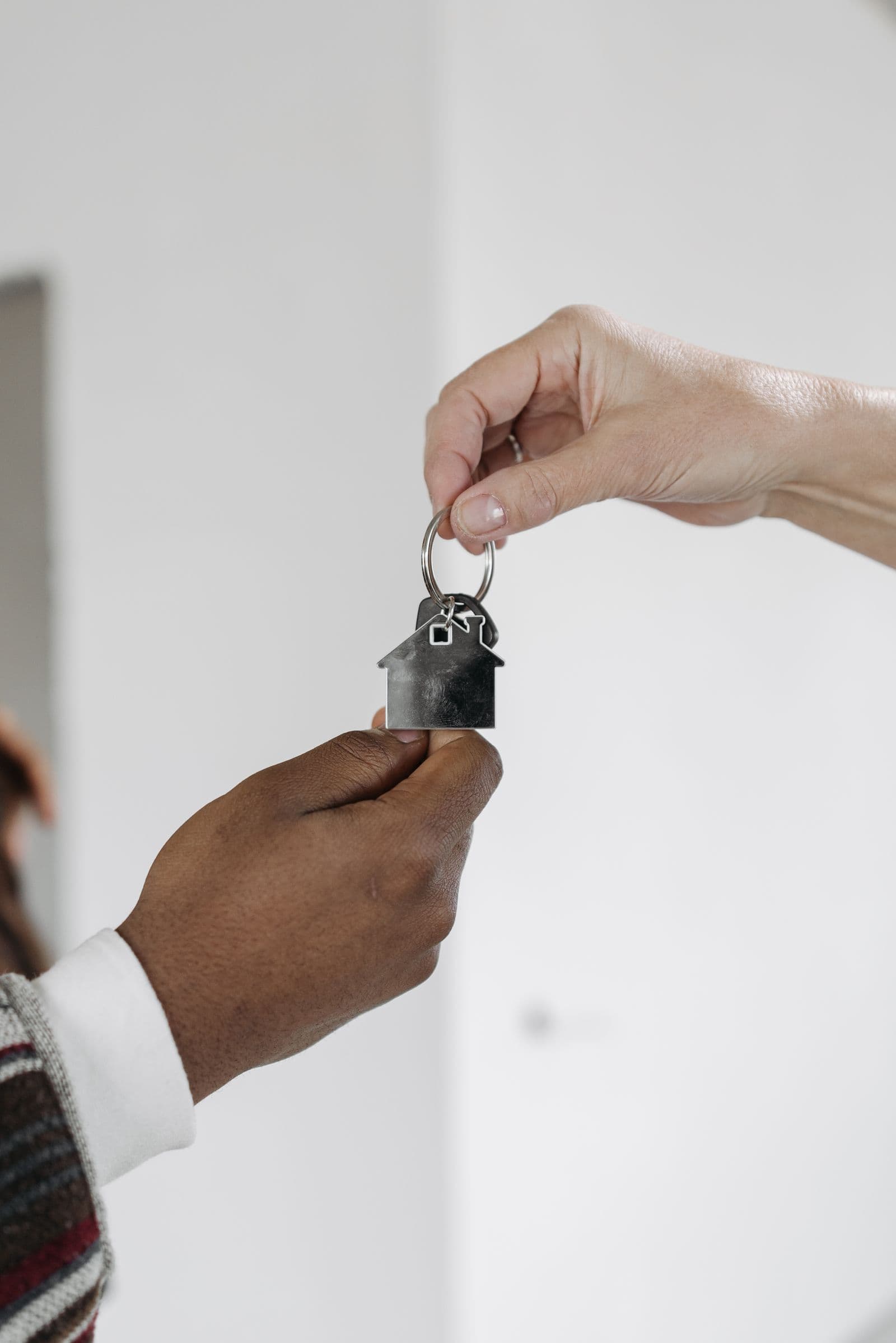 Hands exchanging a key with a house-shaped keyring